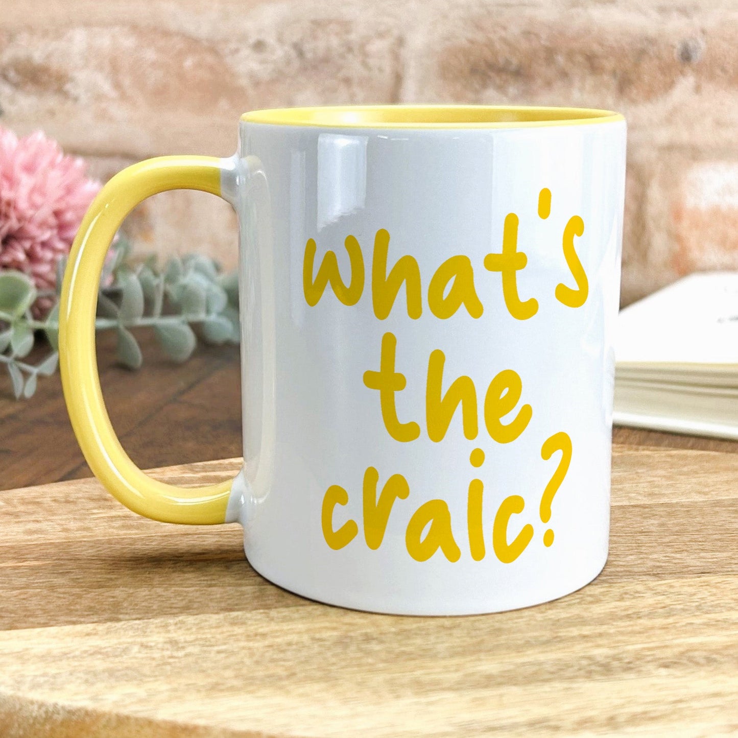 a yellow and white coffee mug with what's the craic? written