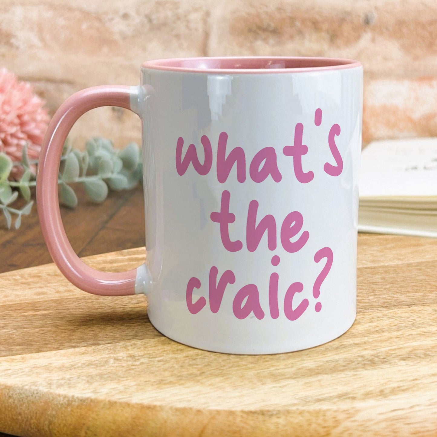 a pink and white coffee mug that says what's the craic?