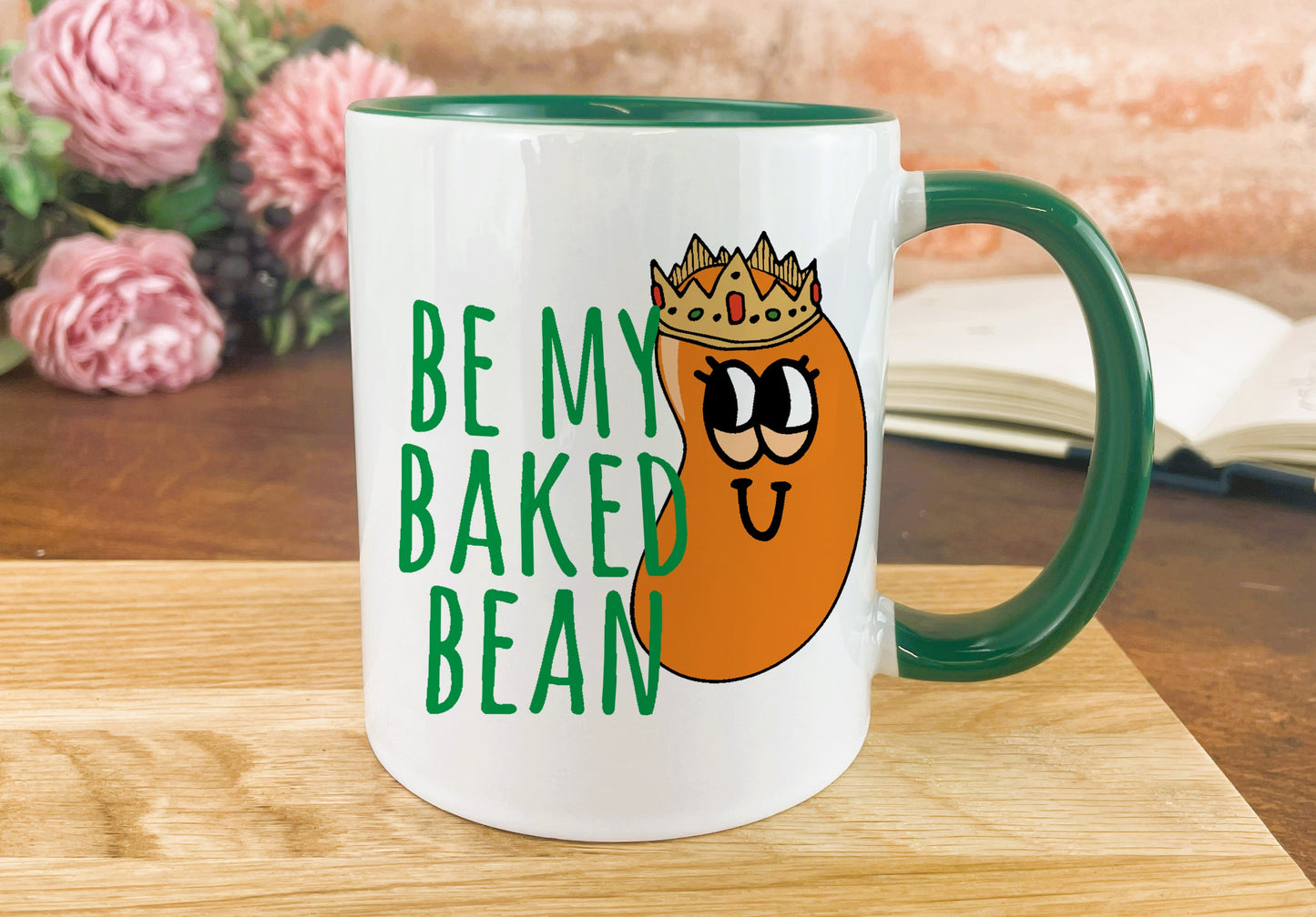 a green and white coffee mug with a picture of a baked bean wearing a crown