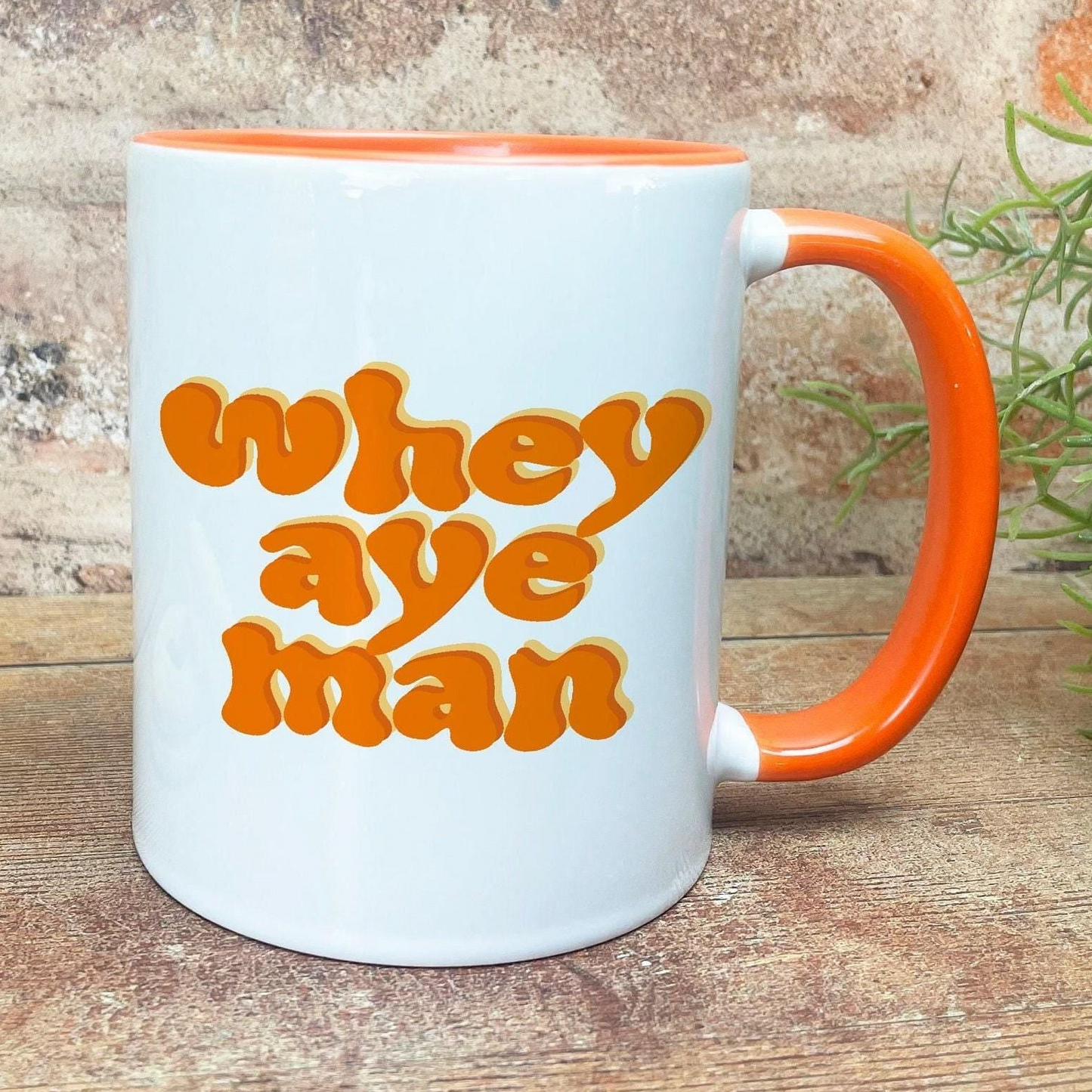 A white mug with an orange handle, featuring the text "whey aye man" in a retro style.
