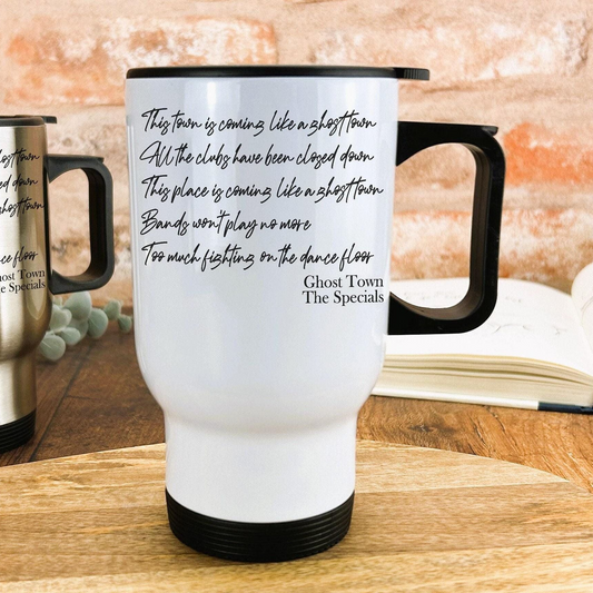 A white travel mug with black text printed on it, placed on a wooden surface.