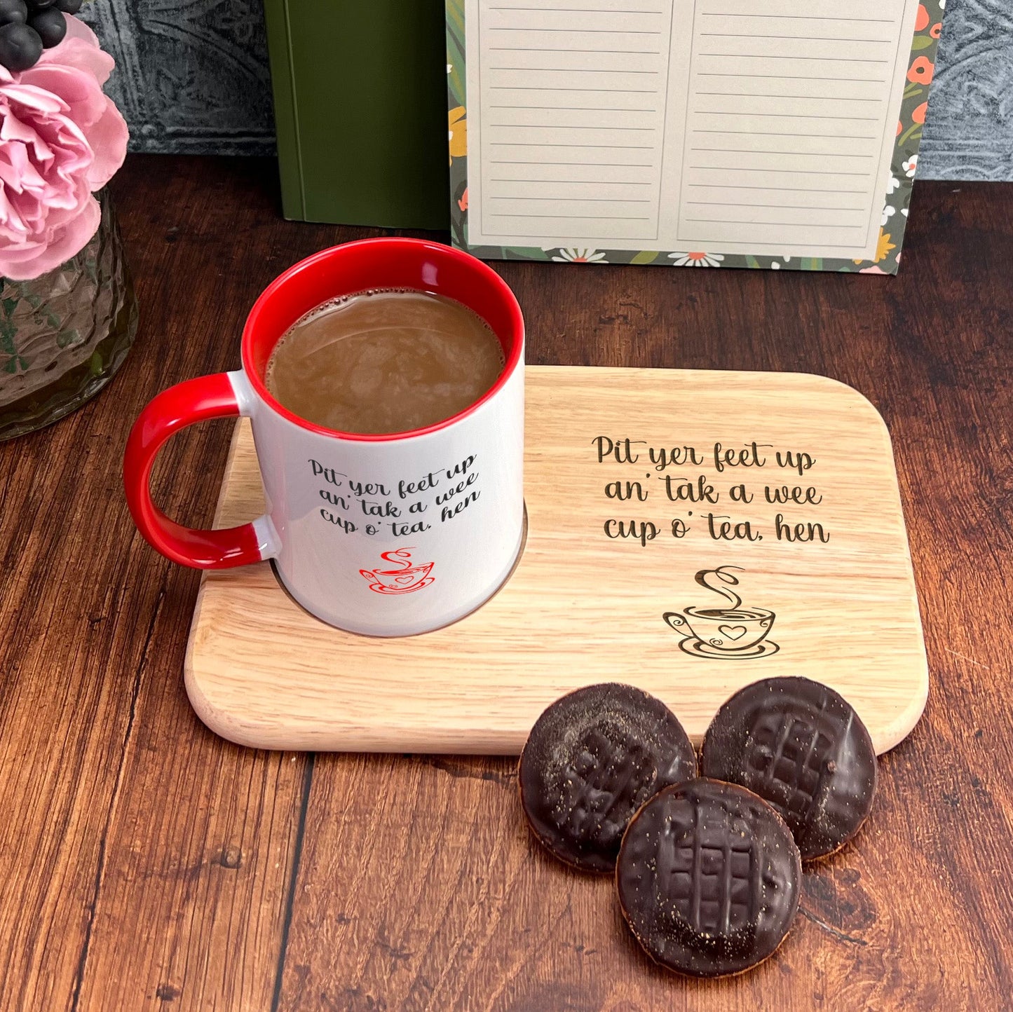 A wooden tray with a message about coffee and tea, a mug, and three chocolate cookies on a wooden surface.