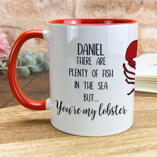 A white mug with a red handle, featuring a red lobster and text that reads "Daniel, there are plenty of fish in the sea but you're my lobster".