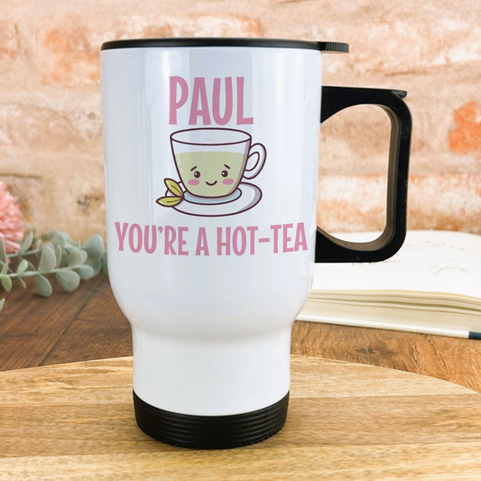 A white travel mug with a black handle, featuring a cartoon cup of tea and the text "PAUL YOU'RE A HOT-TEA" printed on it.