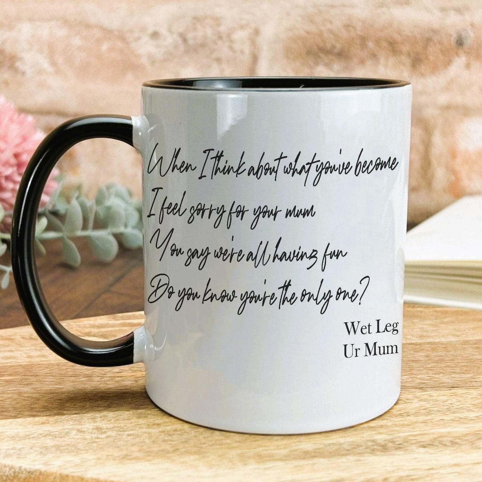 A white mug with black text printed on it, placed on a wooden surface.