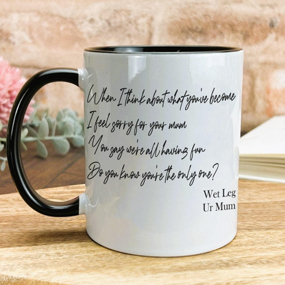 A white mug with black text printed on it, placed on a wooden surface.