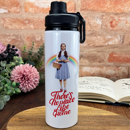 A white water bottle with a printed image of a woman and the text "There's No Place Like Home" on it, placed on a wooden surface next to a book and some flowers.