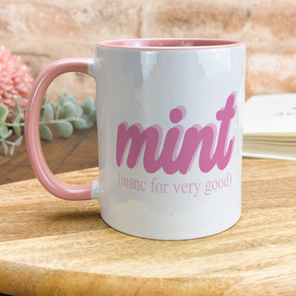 a pink and white coffee mug sitting on top of a wooden table