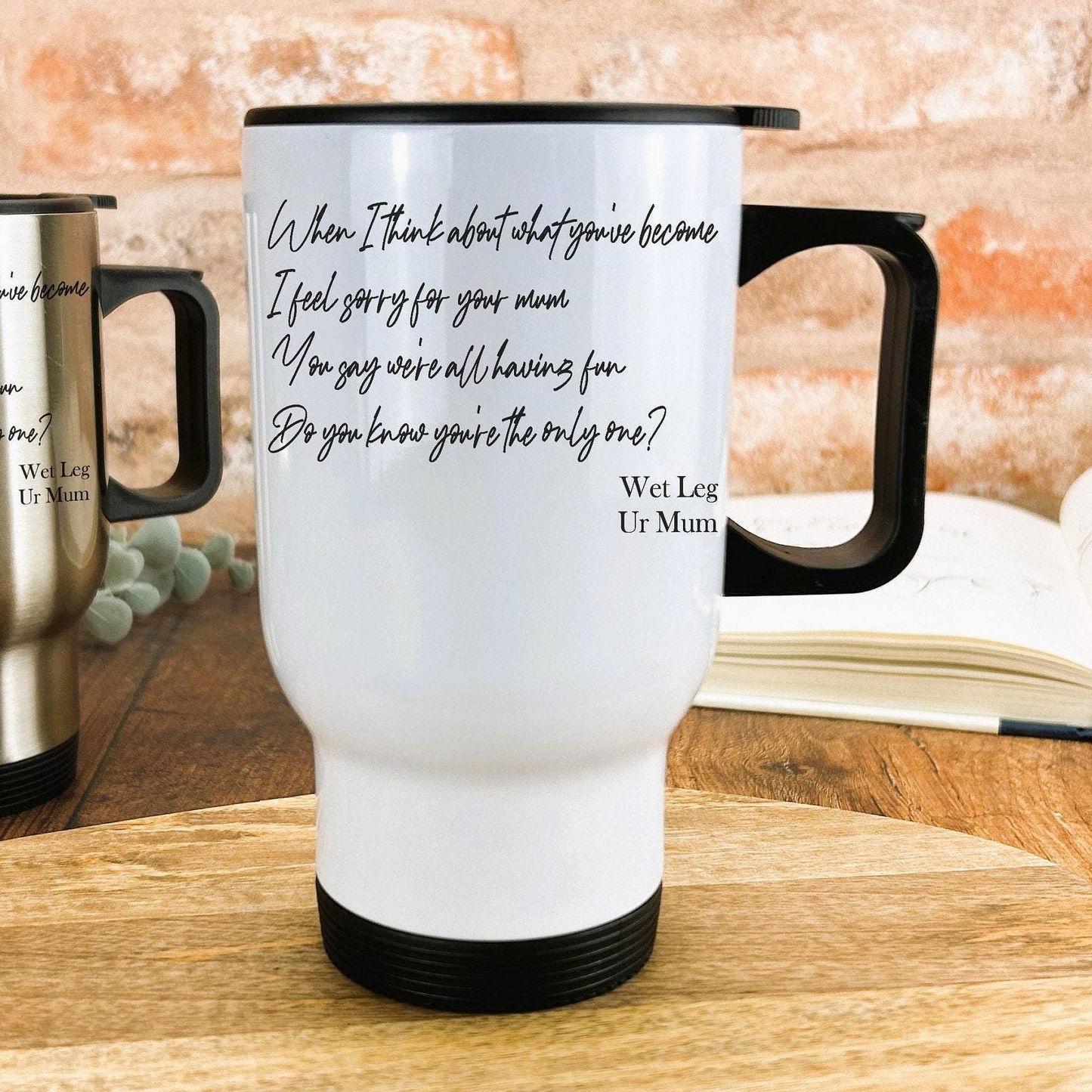 A white travel mug with black text and a humorous message, placed on a wooden surface.