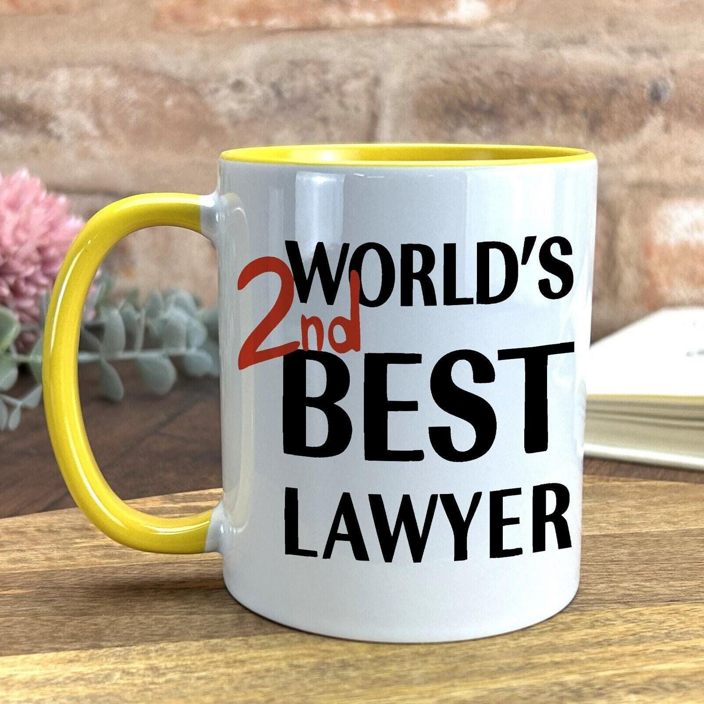 A white mug with a yellow handle, featuring the text "WORLD'S 2ND BEST LAWYER" printed on it.