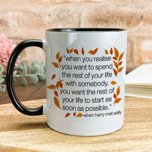 A white mug with a quote about spending the rest of one's life with someone, surrounded by autumn leaves, placed on a wooden surface.
