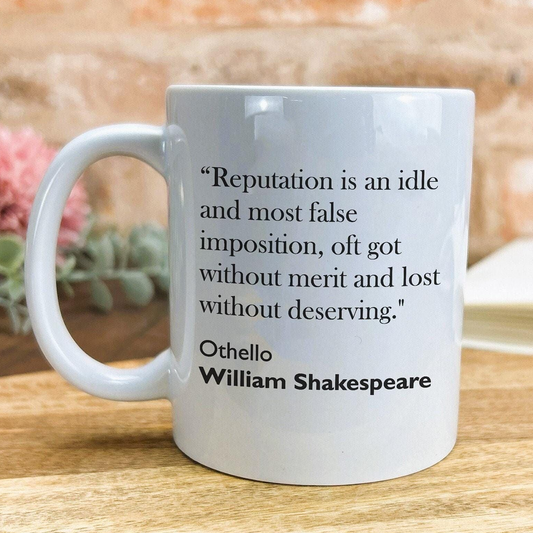 A white ceramic mug with a quote from William Shakespeare printed on it, placed on a wooden surface.