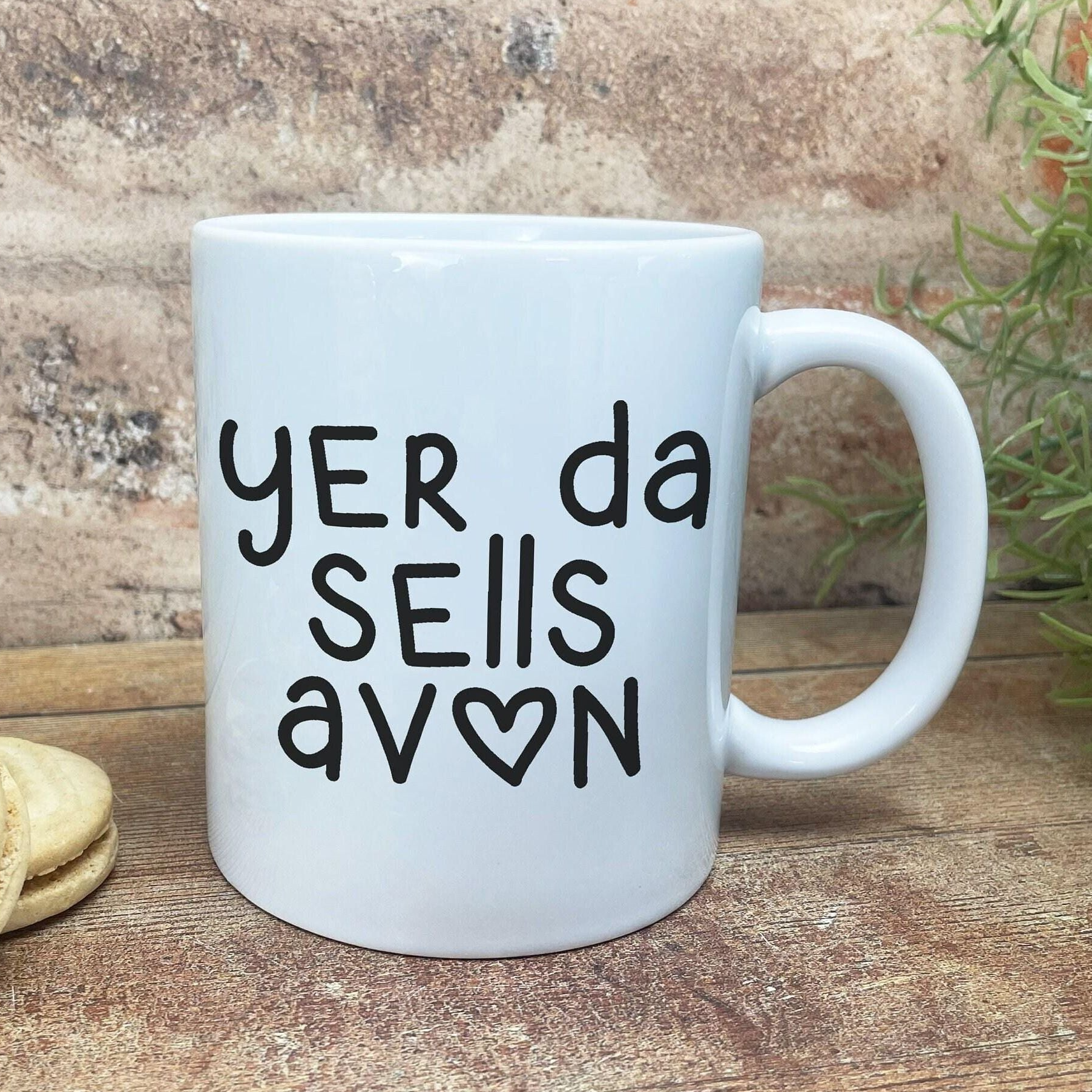A white ceramic mug with black text printed on it, sitting on a wooden surface.