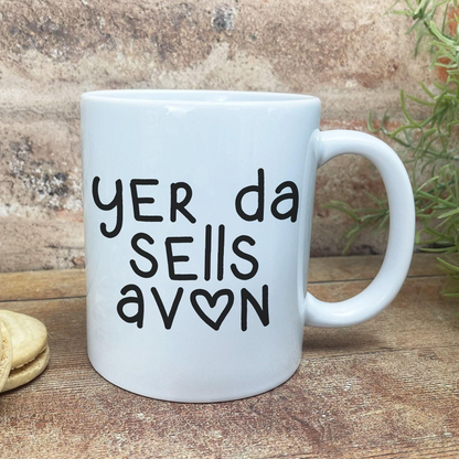 A white ceramic mug with black text printed on it, sitting on a wooden surface.