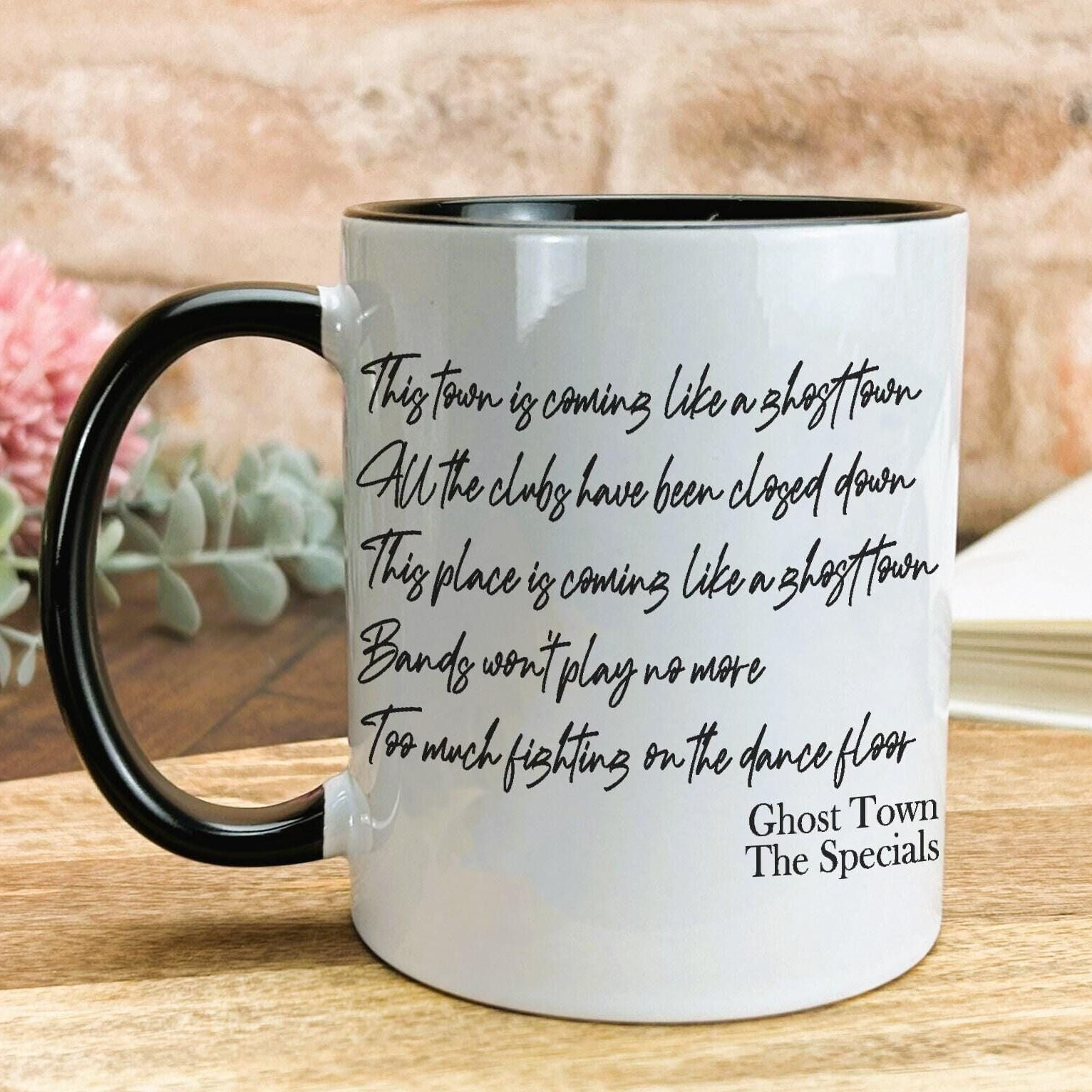 A white coffee mug with black text printed on it, placed on a wooden surface.