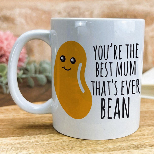 A white ceramic mug with a cartoon bean design and text printed on it.