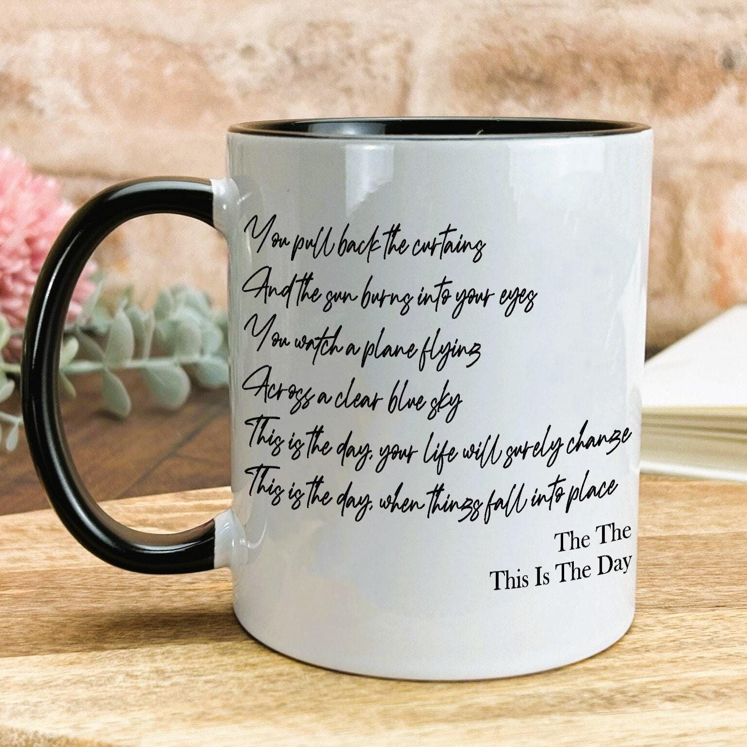 A white mug with black text printed on it, sitting on a wooden surface.
