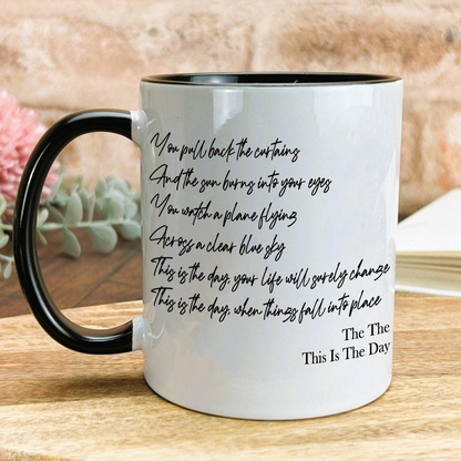 A white mug with black text printed on it, sitting on a wooden surface.