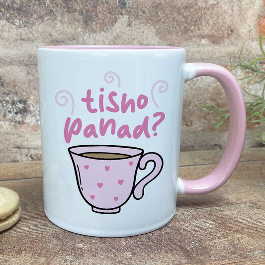 A white mug with a pink handle, featuring a cartoon illustration of a teacup with hearts on it, and the text "tisho panad?" written above it.