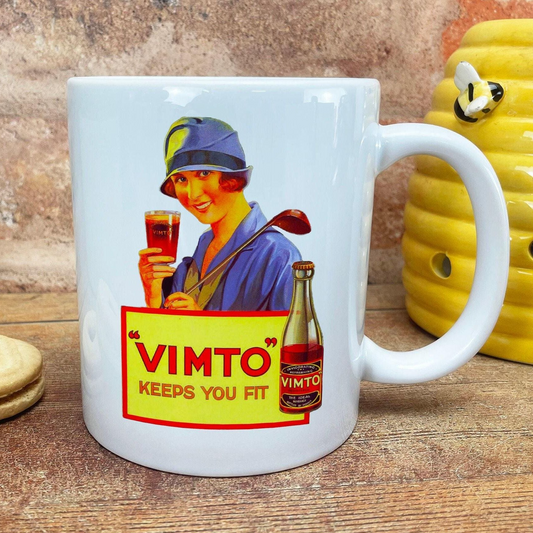 A white ceramic mug with a vintage advertisement featuring a woman holding a glass of wine and a bottle of VIMTO.