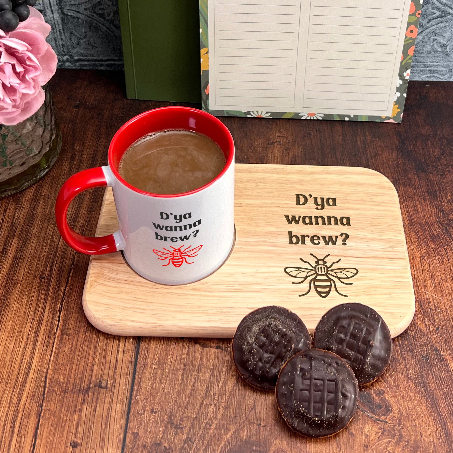 A mug with the text "D'ya wanna brew?" and a wooden tray with three chocolate cookies are placed on a wooden surface.