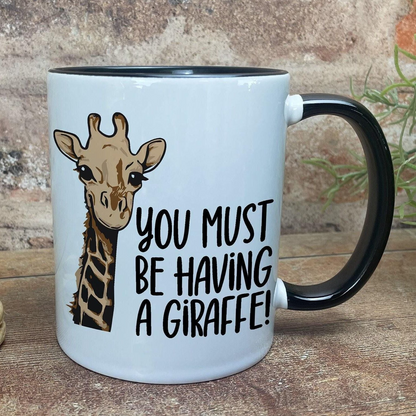 A white mug with a black handle, featuring an illustration of a giraffe and the text "You MUST BE HAVING A GIRaffe!"