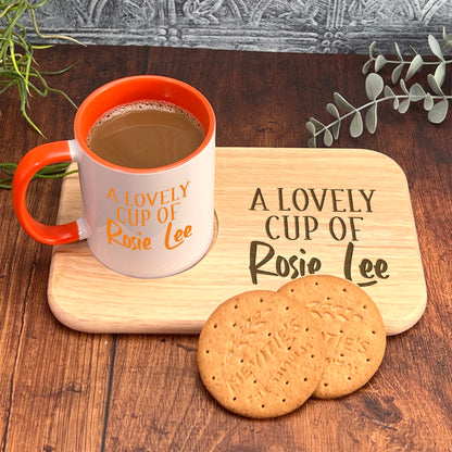 A white mug with an orange rim and the text "A LOVELY CUP OF Rosie Lee" sits on a wooden tray, accompanied by two round cookies.