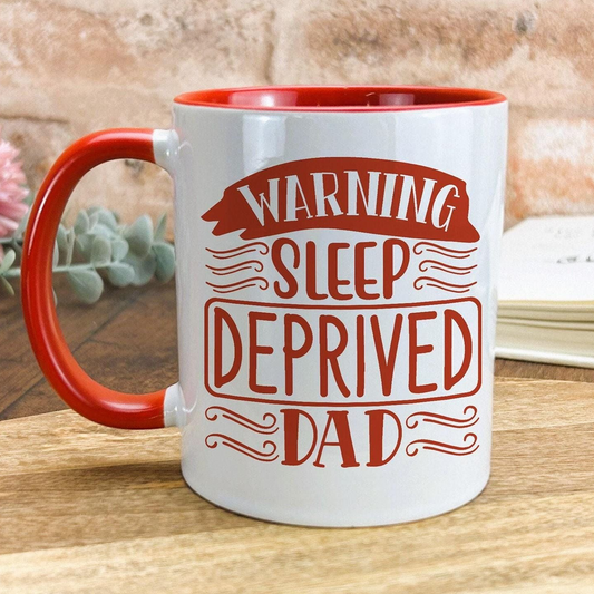 A white mug with a red rim, featuring a red and white design that says "WARNING SLEEP DEPRIVED DAD".