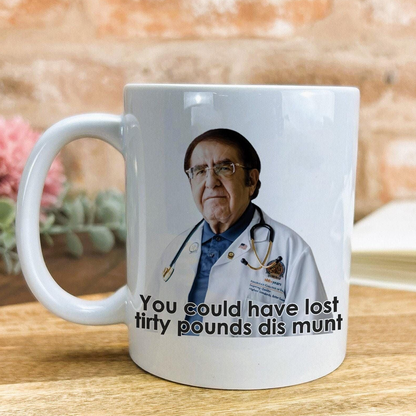 A white ceramic mug with a printed image of a man wearing a white coat and stethoscope, along with the text "You could have lost filthy pounds dis munt" printed on it.