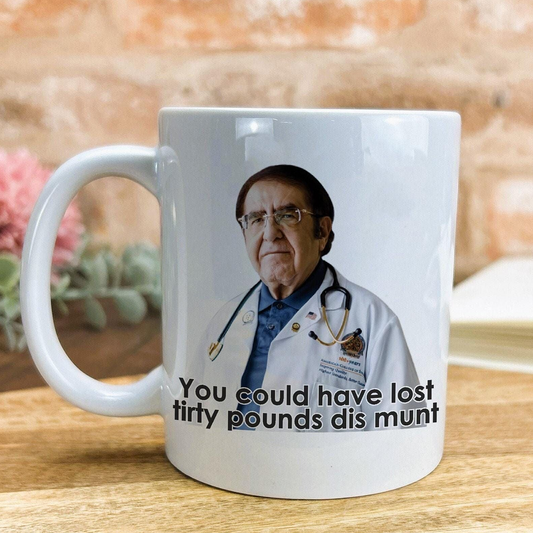 A white ceramic mug with a printed image of a man wearing a white coat and stethoscope, along with the text "You could have lost filthy pounds dis munt" printed on it.