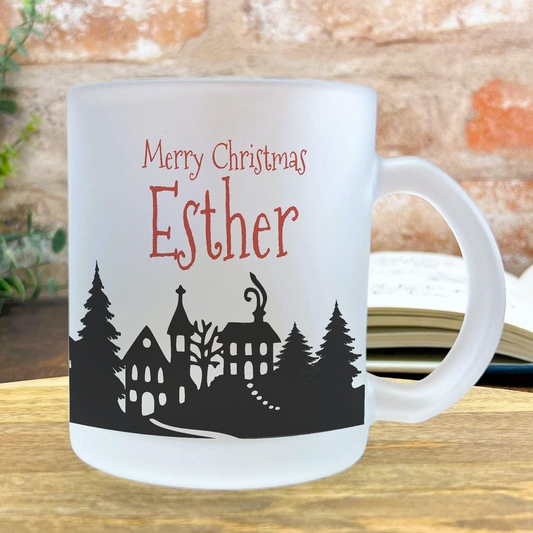 A white ceramic mug with a black silhouette of a village and trees, along with the text "Merry Christmas Esther" printed on it.