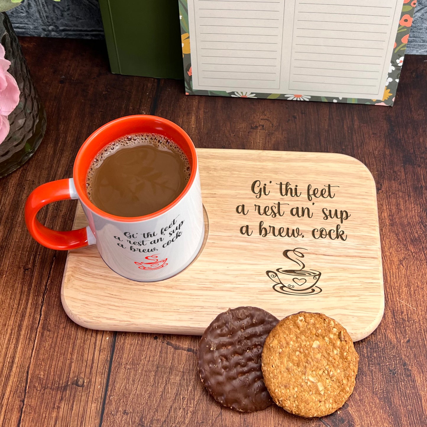 A wooden tray with a mug of coffee and two cookies, accompanied by a note that reads " Gi' thi feet a rest an sup a brew, cock".