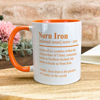 an orange and white coffee mug sitting on top of a wooden table