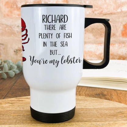 A white travel mug with a black handle, featuring a red lobster and text that reads "RICHARD THERE ARE PLENTY OF FISH IN THE SEA BUT... You're my lobster".