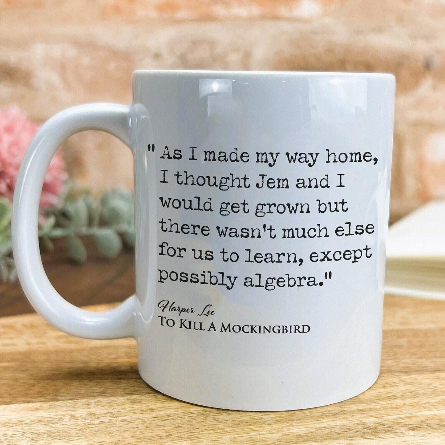 A white ceramic mug with a quote from the novel "To Kill a Mockingbird" printed on it, placed on a wooden surface.