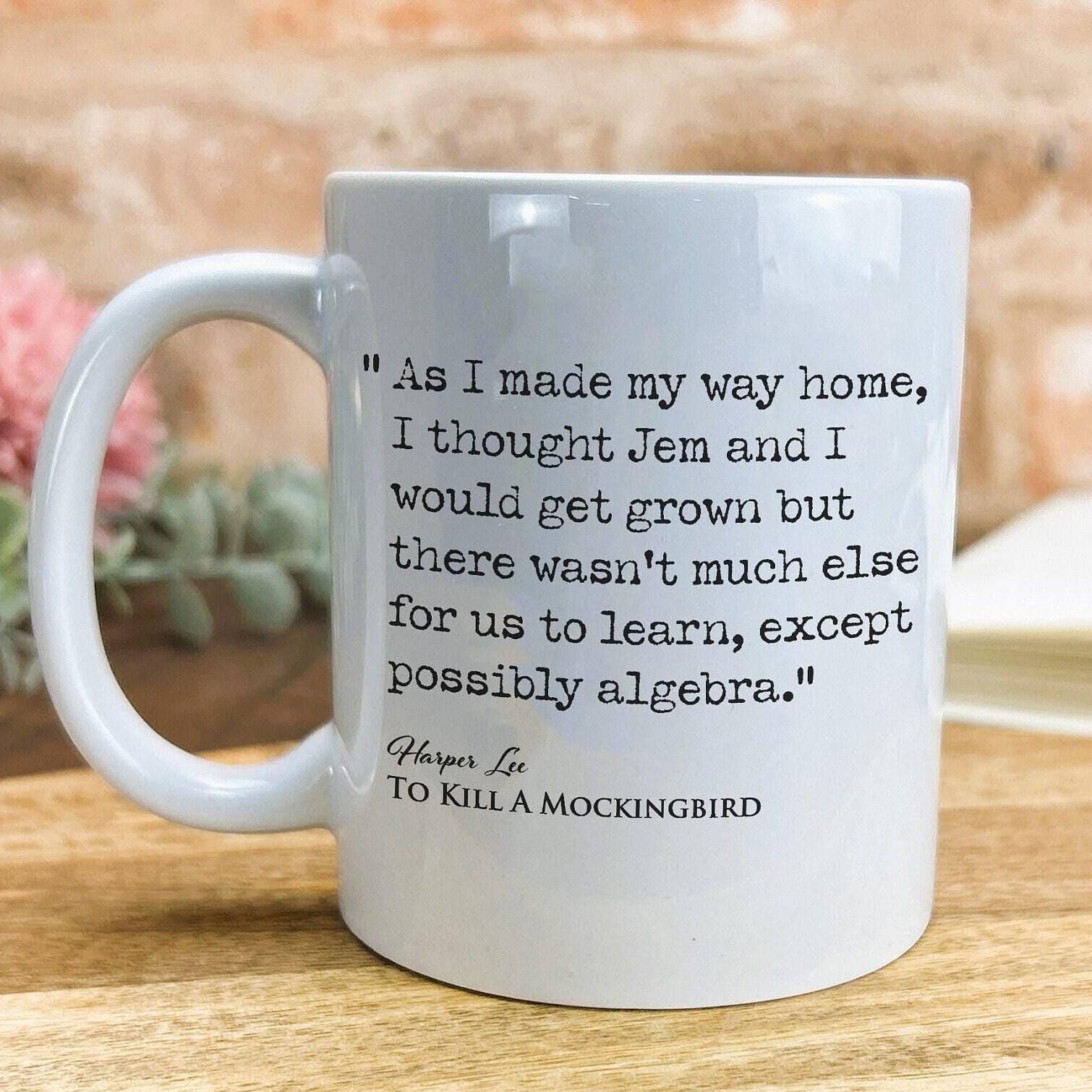 A white ceramic mug with a quote from the novel "To Kill a Mockingbird" printed on it, placed on a wooden surface.