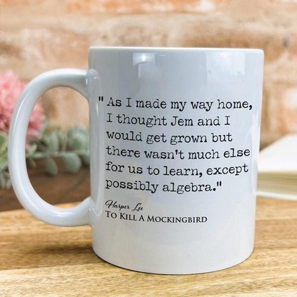 A white ceramic mug with a quote from the novel "To Kill a Mockingbird" printed on it, placed on a wooden surface.