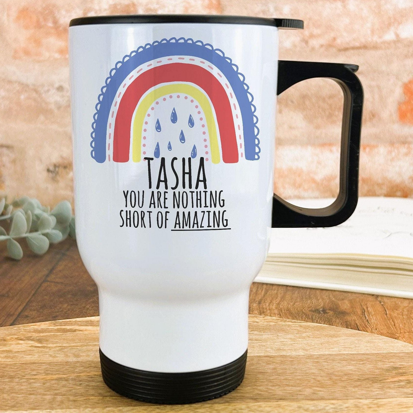 A white travel mug with a black handle, featuring a colorful rainbow design and the text "Tasha, you are nothing short of amazing" printed on it.