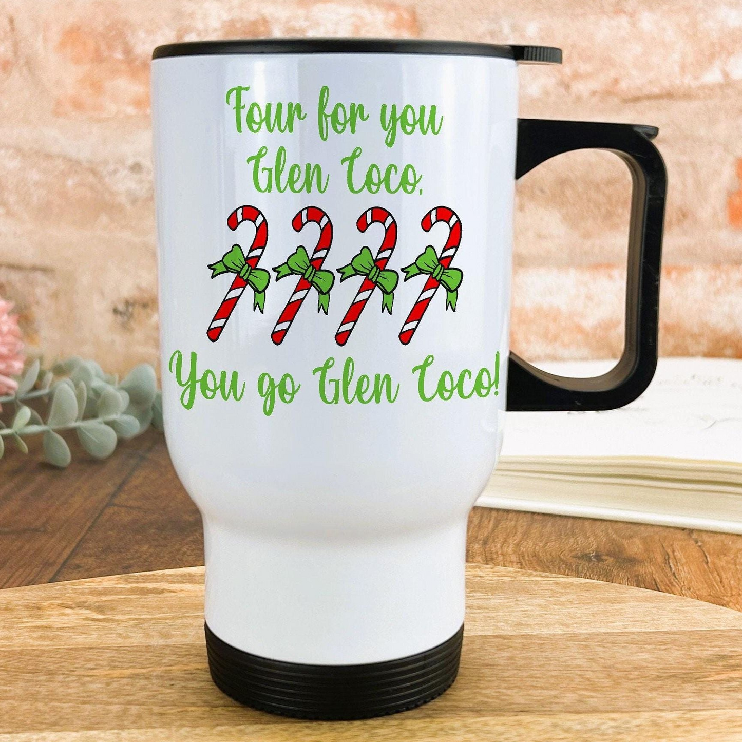 A white travel mug with a black handle, featuring a humorous text and candy cane design.
