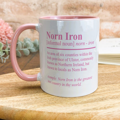 a pink and white coffee mug sitting on top of a wooden table