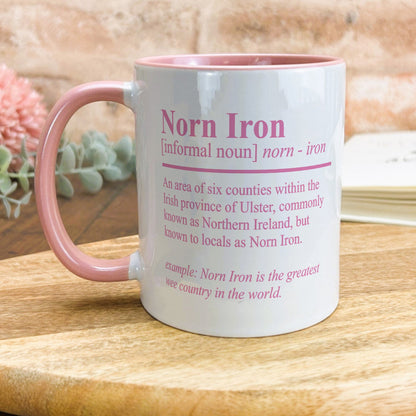a pink and white coffee mug sitting on top of a wooden table