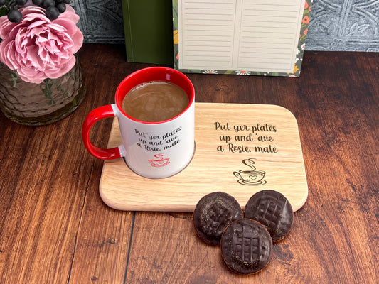A wooden tray with a message about putting plates up and a mug of coffee, accompanied by three chocolate cookies on a wooden surface.