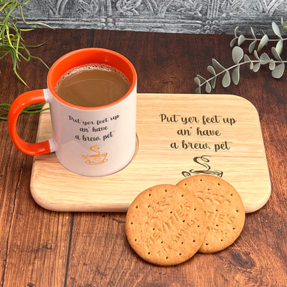 A wooden tray with a mug of coffee and two cookies on it, accompanied by a plant and a wooden board with a message about putting one's feet up.