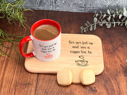 A red and white mug filled with coffee sits on a wooden tray, accompanied by a small plant and some cookies, with a wooden board displaying a humorous message.