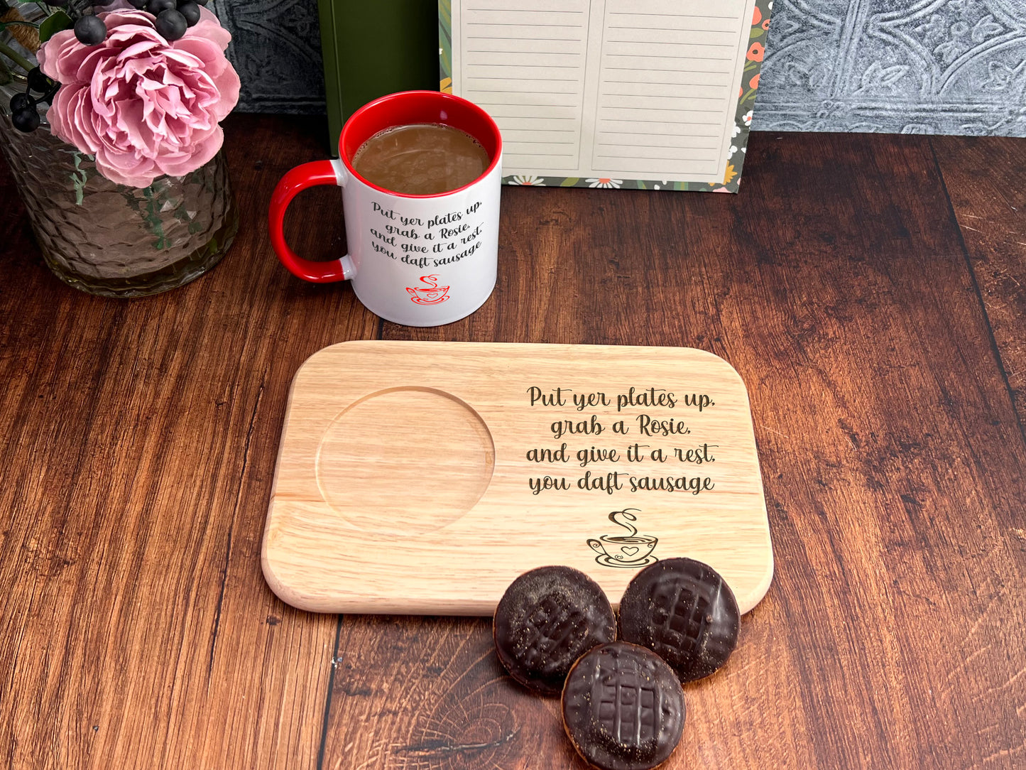 a wooden tray with a message about sausage, a mug of coffee, and a vase of pink flowers on a wooden table.