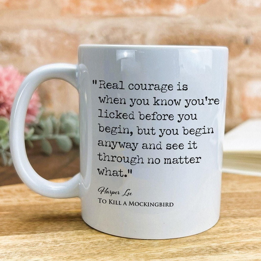 A white ceramic mug with a quote from the novel "To Kill a Mockingbird" by Harper Lee printed on it.