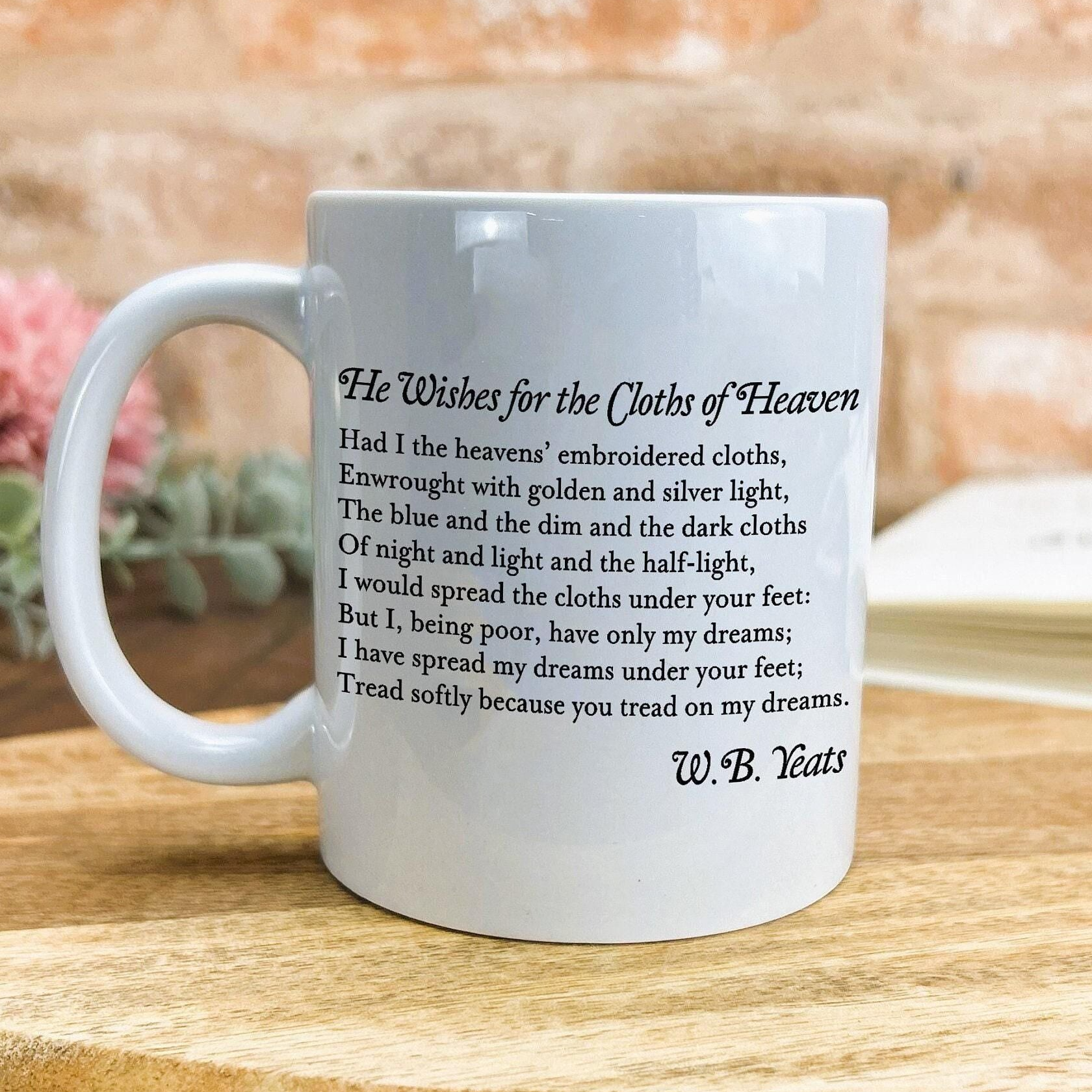 A white ceramic mug with a printed poem or lyrics on it, placed on a wooden surface.