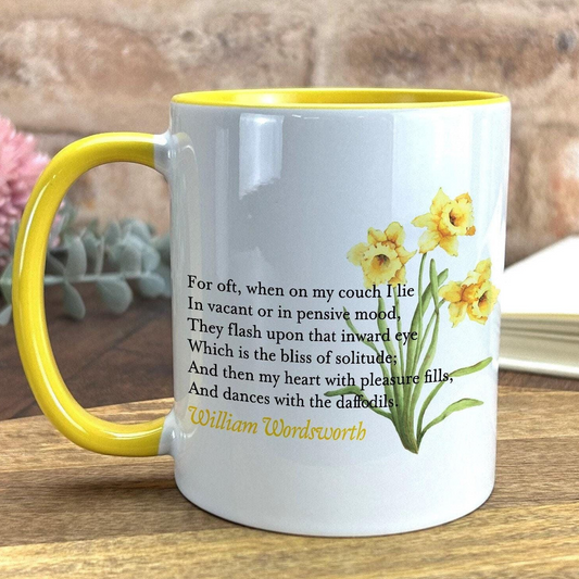 A white ceramic mug with a yellow rim, featuring a printed design of yellow daffodils and a poem by William Wordsworth.