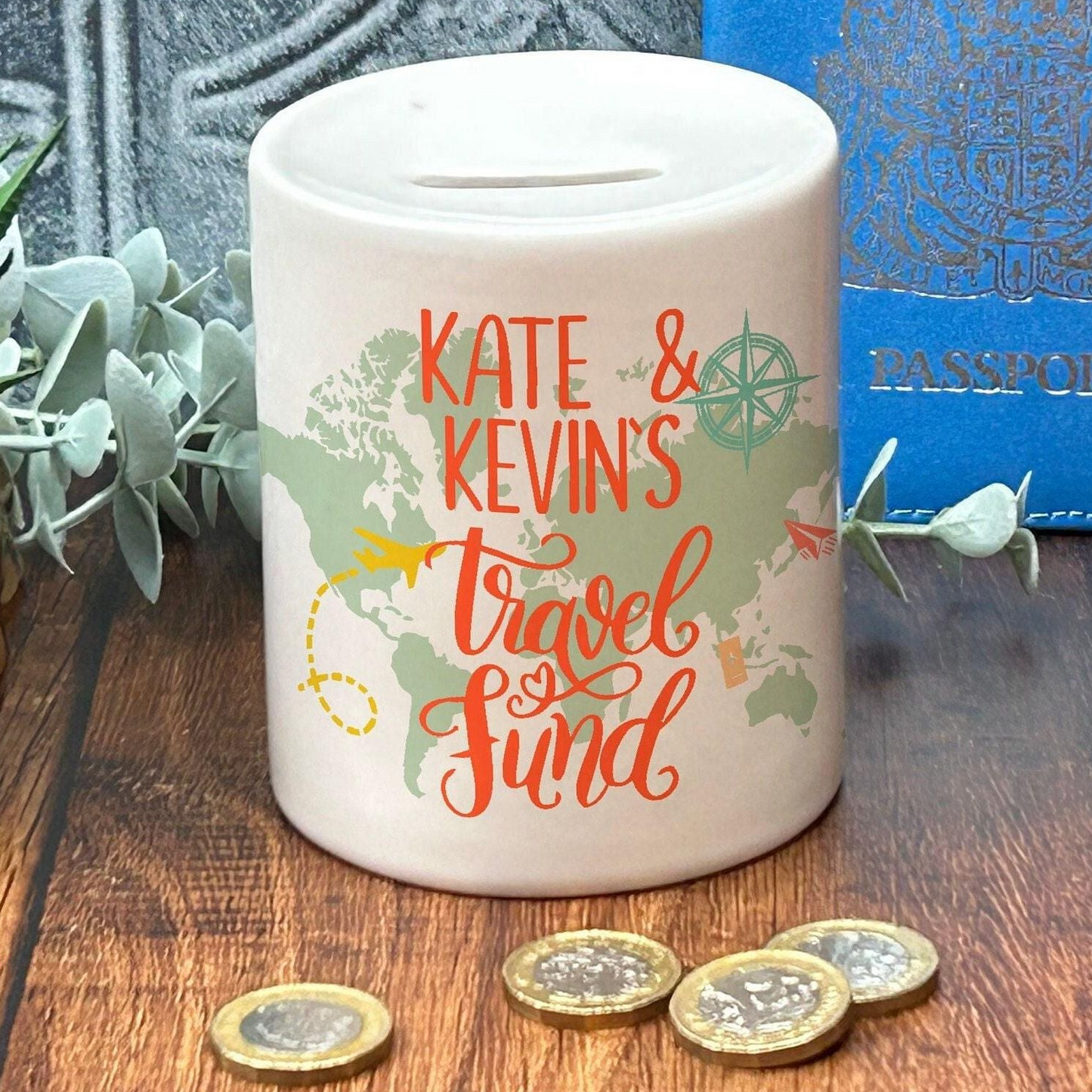 A white ceramic travel fund jar with the text "KATE & KEVIN'S TRAVEL FUND" printed on it, placed on a wooden surface with some coins and a passport visible in the background.