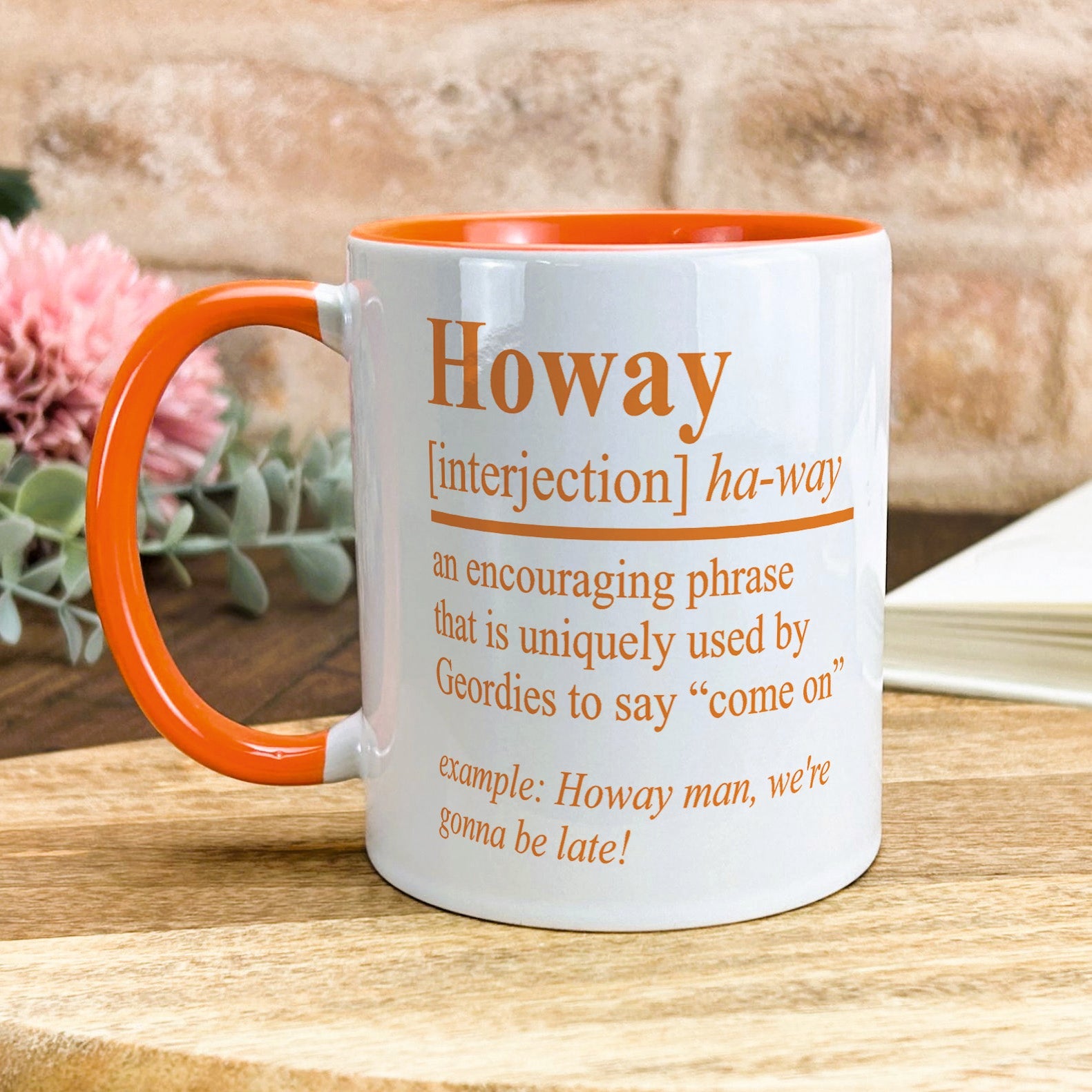 a coffee mug sitting on a table next to a pink flower